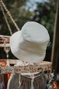 Cappellino da pescatore da bambino del brand Primi Vizi color bianco panna appeso a una struttura metallica 