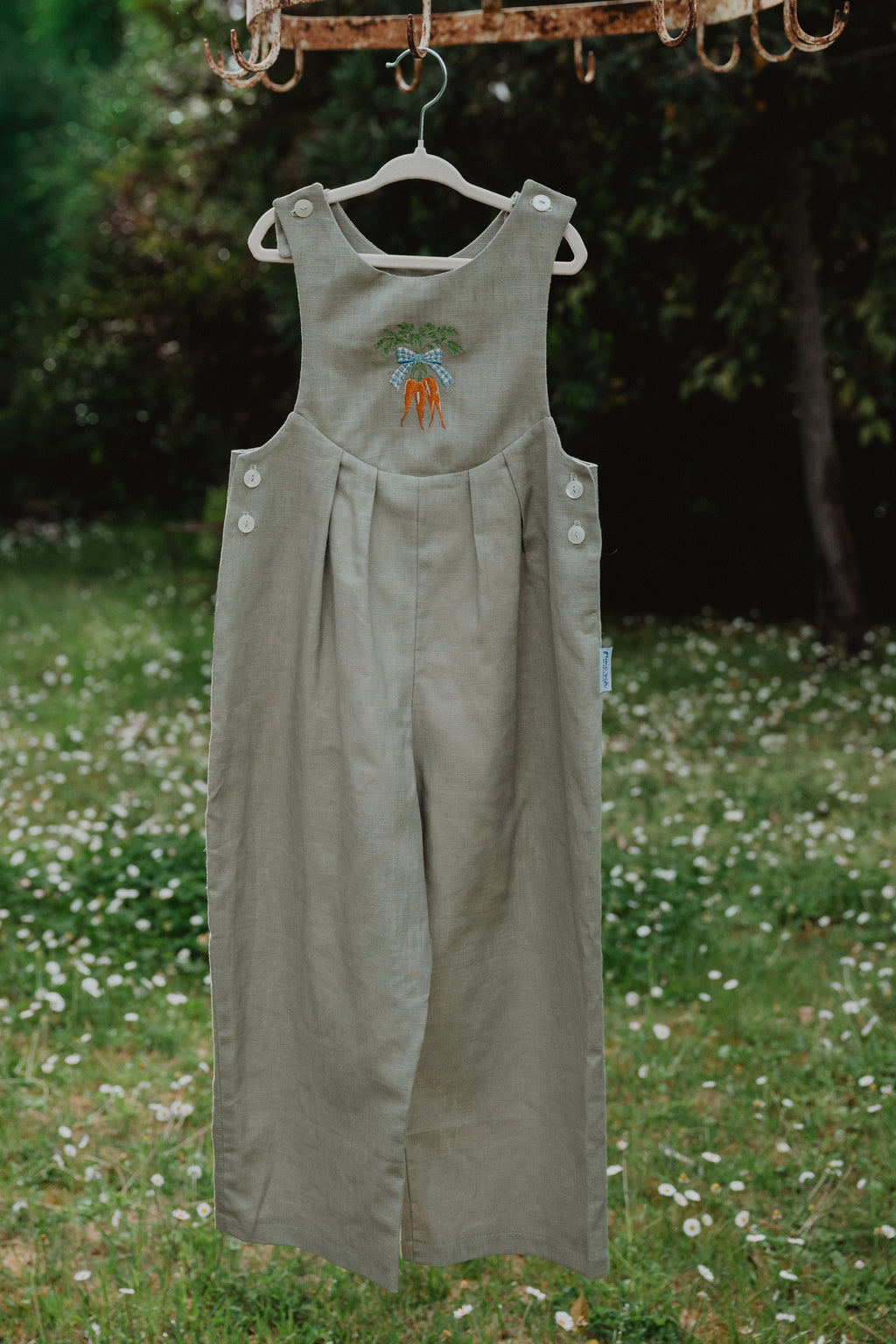 Salopette unisex in lino lavato oliva chiaro appesa, con ricamo carote e bottoni