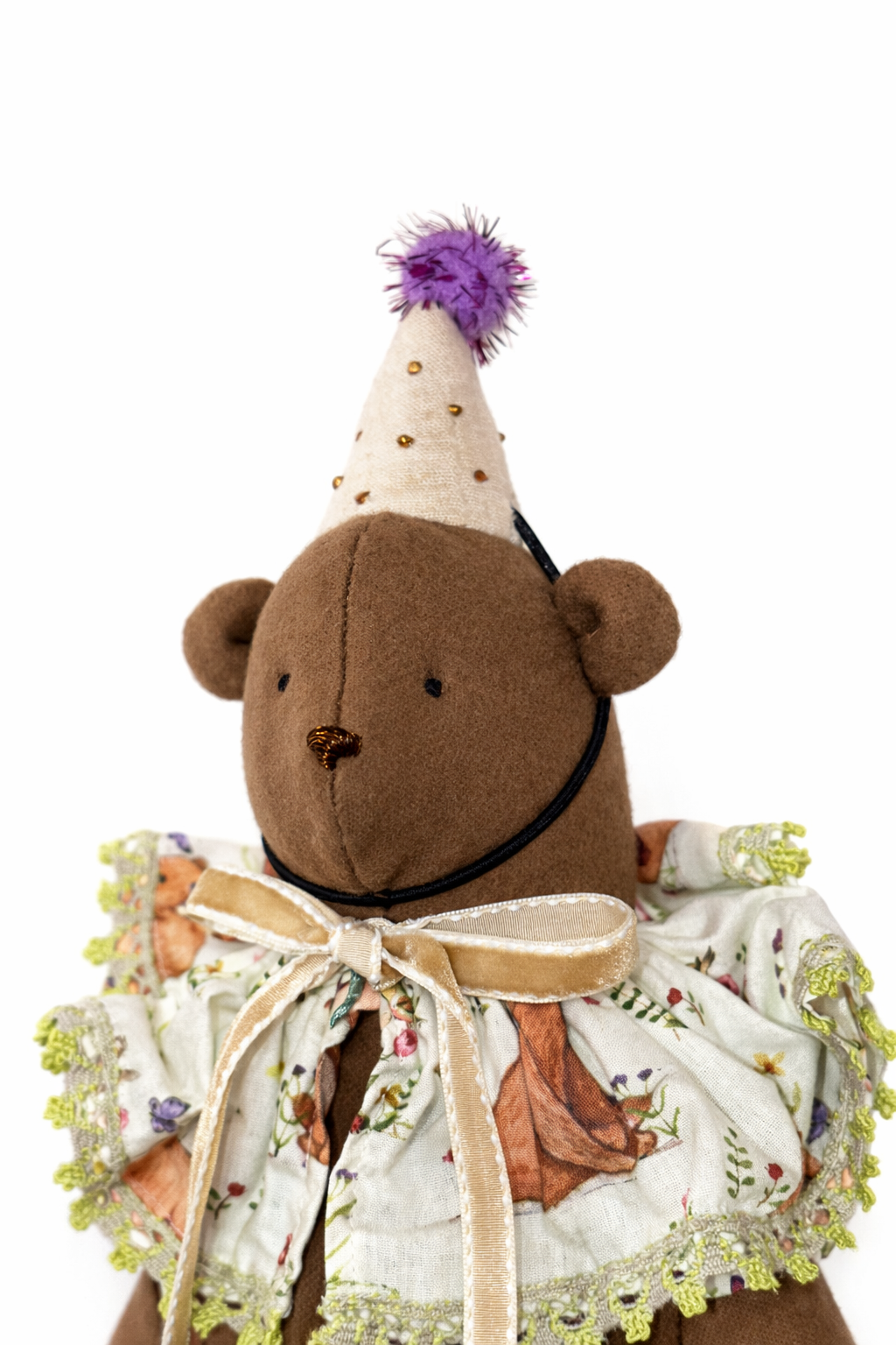 Orsetto di peluche marrone con cappello viola e fiocco beige sul vestitino