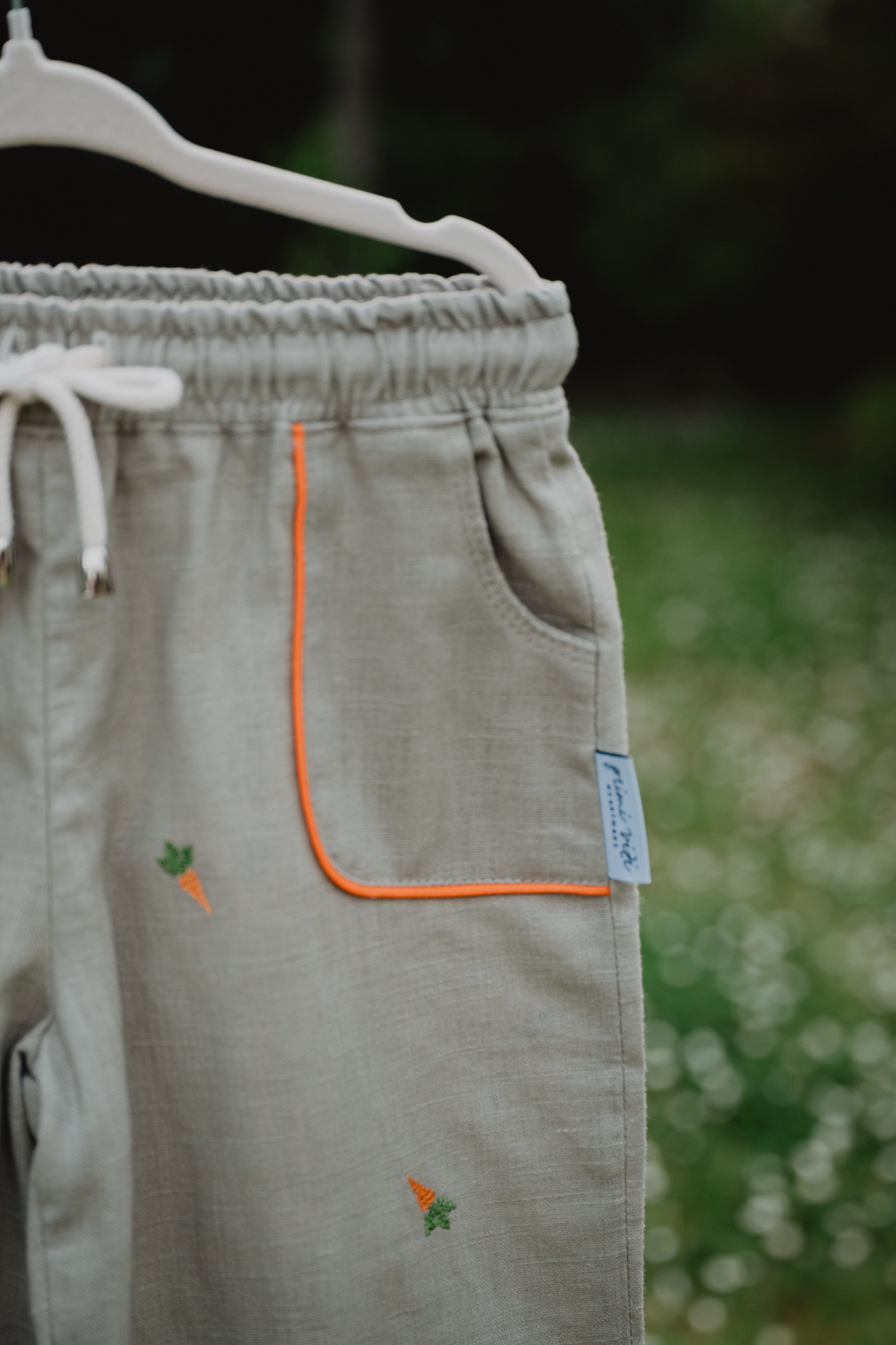 Pantaloni baggy chiari in lino con coulisse, tasca arancione e ricamo a carota